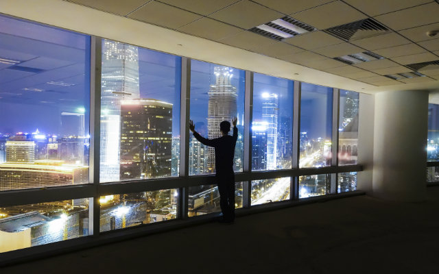 Image of a man standing in front of a window with a cityscape at night
