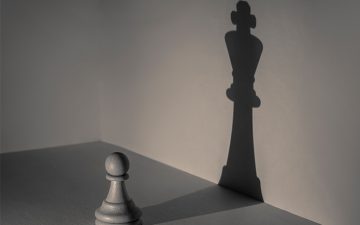 Chess pawn piece casting the shadow of a chess king piece