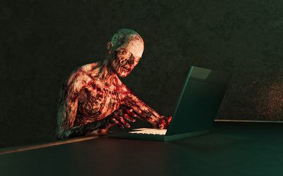 Horror Zombie with flaking flesh using laptop computer in dark room.